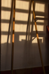 Two broomsticks against a wall with the shadow of a window casted by the light of the sunset, in a...