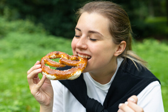 Young happy woman eating a german pretzel in the park