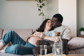Diverse pregnant couple In Love Cuddling On The Sofa