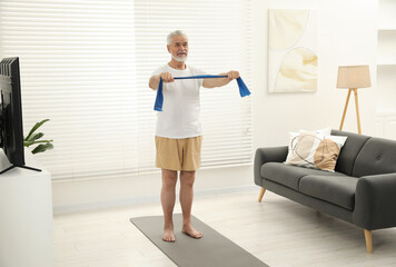 Fototapeta na wymiar Senior man doing exercise with fitness elastic band on mat at home