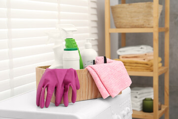 Different cleaning products in wooden box on washing machine indoors
