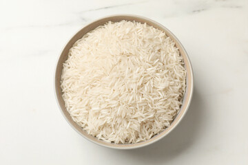 Raw basmati rice in bowl on white marble table, top view