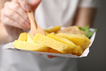 Woman eating delicious fish and chips on gray background, closeup