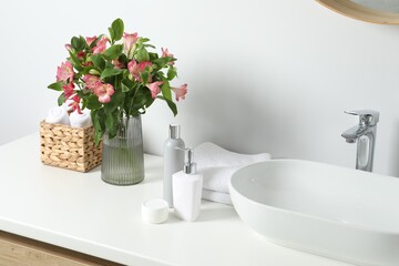 Vase with beautiful Alstroemeria flowers and toiletries near sink in bathroom
