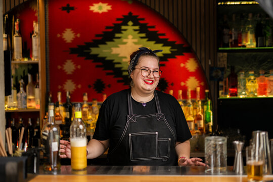 Portrait of young cheerful female bartender looking at camera in a bar