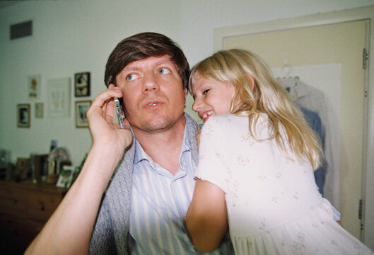 Man talking on the phone at home wth a daughter on his hands