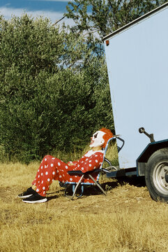 man wearing a clown costume sitting next to a caravan, 35mm