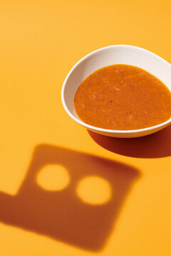 a plate of tomato soup with the shadow of a piece of bread