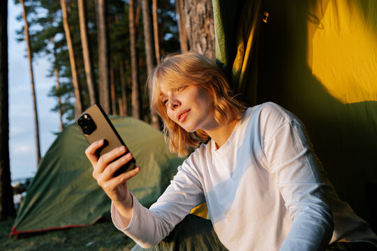 A woman uses a mobile phone sitting in a camping