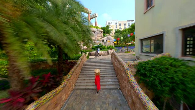 FPV of young woman in a red dress and Vietnamese hat exploring Sunset Town on Phu Quoc Island, Vietnam.