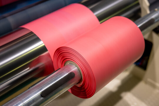 Roll of red polyethylene film for bags and packaging. Extrusion line for the production of polyethylene film for products packaging. Winding a polyethylene roll for packaging