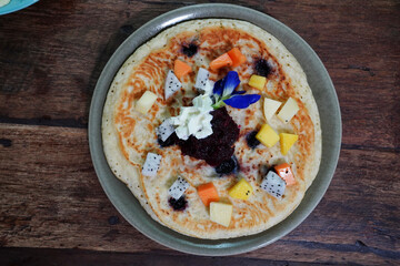 Blueberry Pancakes, Mixed Berry Sauce. topped with whipped cream and syrup. Decorated with fresh flowers and fruit. homemade brunch, served on a plate and placed on wooden table.