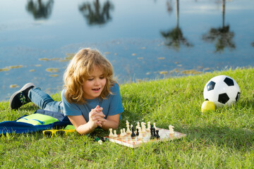 Little kid play chess in park. Child boy playing board game outdoor. Thinking child brainstorming...