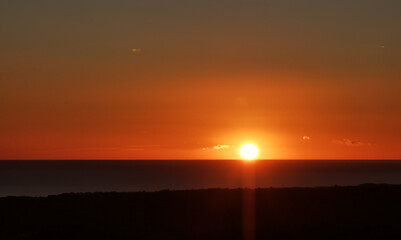 Il Sole accecante che all’alba sorge dal mare visto da sopra le colline 