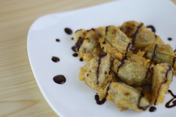 Pisang Goreng Keju or Fried Banana topped chocolate with on white plate on the wooden table.