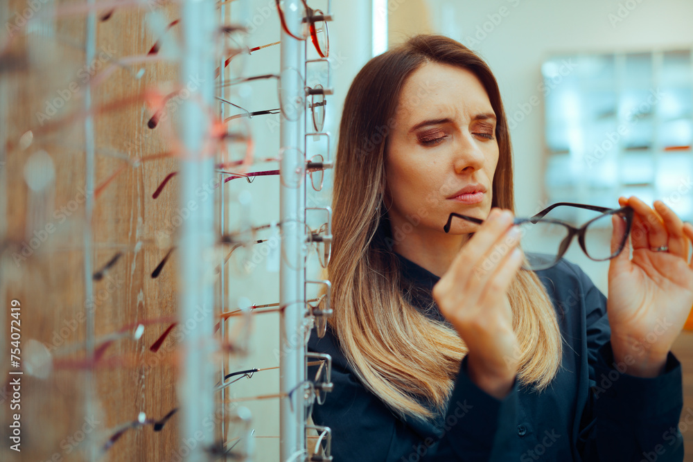 Wall mural skeptical customer trying on eyeglasses in an optical store. frowning woman worried about the qualit