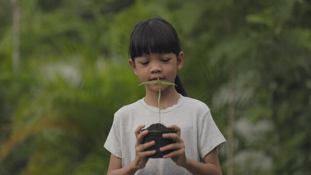 A Thai Asian kid girl, aged 8 to 10 years, has a cute face and a bright smile. She held a pot of seedlings in her hand. trees are going to be planted To care for a sustainable world, Earth Day concept