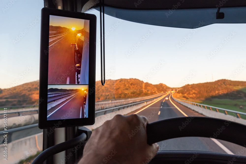 Wall mural View from the driver's position of a truck on the road of a sunrise seen by the vehicle's rearview camera, truck driving on a highway.