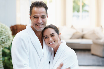Portrait, robe and couple at hotel with embrace, smile and relax together at wellness spa holiday. Hospitality, happy woman and man hug at luxury villa for travel, vacation and love on romantic date - Powered by Adobe