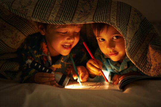 Blanket, flashlight and children at night with happiness in portrait with drawing in a book. Friends, relax and sketch on notebook in dark with light under duvet at sleepover with a pillow tent