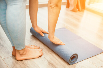 Woman hands rolled up yoga mat on gym floor in yoga fitness training room. Home workout woman close...