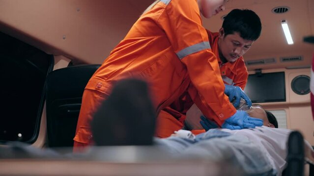 Asian woman emergency medical technician (EMT) or paramedic nurse is performing CPR on a patient in an ambulance car