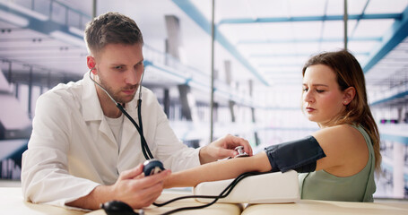 Fototapeta premium Male Doctor Checking Pregnant Woman Blood Pressure