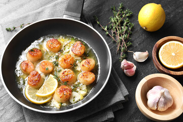 Delicious scallops with sauce in frying pan and ingredients on dark gray textured table, above view
