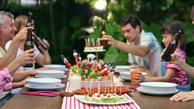 Big family multi-ethnic celebrating outdoors party at garden within the house. Family and friends gathering at the table clink a bottle having dinner party on weekend together in the night.