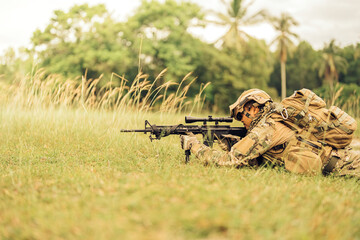 Soldiers from the American Special Forces lie down on a grass field ready to fight with rifles, aiming their barrels, wearing camouflage uniforms and military helmets on an enemy battlefield.