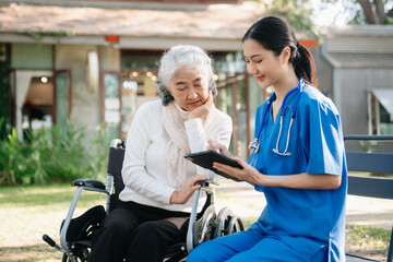 Fototapeta na wymiar Elderly asian senior woman on wheelchair with Asian careful caregiver and encourage patient, walking in garden.