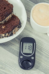 Glucometer with result sugar level, sweet chocolate cake and cup of coffee with milk. Nutrition...