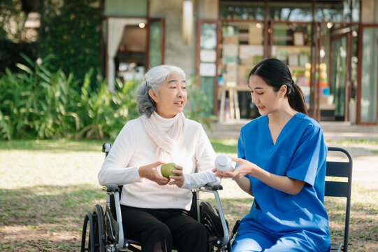 Asian young caregiver nurse support senior older male walking outdoors. Specialis doctor help and take care of elderly mature.
