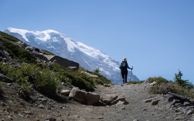 Woman solo hiking Sunrise Trail in summer. Snow-capped Mount Rainier looming large in front....