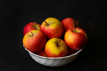 Nature morte of red apples in white bowl on black background