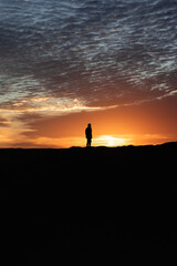 Silhouette of a person watching the sunrise on a dune in the desert of Morocco
