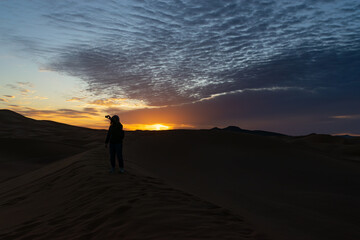 Fototapeta na wymiar A Person taking a selfie at sunrise on a dune in the desert in Morocco