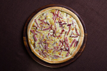 Top view of a pizza on a wooden cutting board with a brown background