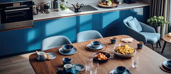 A cozy kitchen with blue walls and a wooden table, adorned with velvet armchairs and a glass table lamp. The sink, induction hob with a pot,