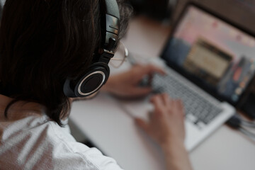 Side view of focused male musician in white t shirt and headphones typing on laptop while recording...