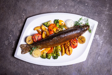 Trout fish with grilled vegetables on a white plate. Isolated on a black background.