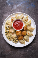 Uzbek samsas and manti with meat, pumpkin and greens on a plate with red sauce