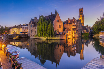 Reflection of the historic buildings from the canal of the Rosary Quay in the Hanseatic city of Bruges. Belfry of the old town and historic guild houses and merchant houses in an evening atmosphere. - obrazy, fototapety, plakaty