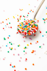 Colorful confectionery sprinkles in iron spoon on white background. Decoration for cake and bakery.
