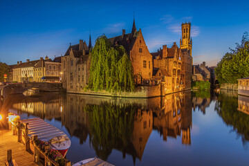Center of old town Bruges. Belgian Hanseatic city in the evening with the Rosary Quay canal at blue hour. Reflections on the water surface. Old illuminated merchant houses with belfry - obrazy, fototapety, plakaty
