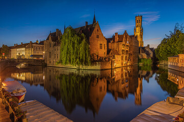 Rosary Quay at the evening in Bruges. Center of the old Hanseatic city with canal at blue hour. Reflections of illuminated historic merchant houses and belfry on the water surface