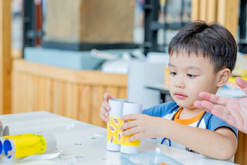 Little asian boy making tissue paper core binoculars. Reuse waste products. Idea custom made toy. Soft focus. Copy space.