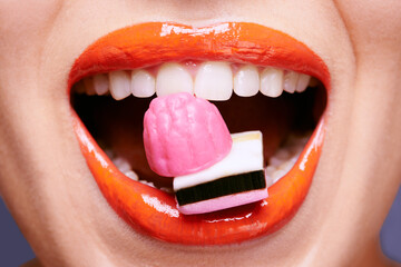 Obraz premium Beauty, lipstick and woman with sweets in mouth, makeup and creativity with closeup of shiny cosmetic product. Licorice, candy and orange lip gloss for aesthetic, art and cosmetology with glamour