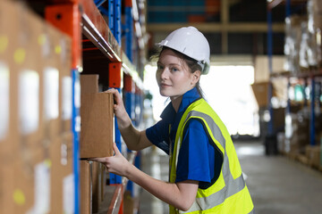 woman professional worker wearing safety uniform and hard hat holding box product on shelves in...