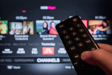 Man using remote control to watch a movie streaming service on TV. Video-on-demand subscription service and platform on television. Stream series, films and shows online. - obrazy, fototapety, plakaty